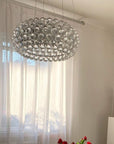 Modern chandelier hanging in a room with light curtains and decorative flowers.