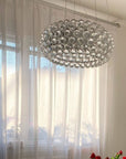 Modern chandelier hanging in a room with light curtains and decorative flowers.