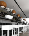 Modern interior with black tiled wall, white bar stools, and decorative ceiling lights.
