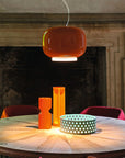 Round wooden table with orange pendant light and decorative items in a room with a fireplace.