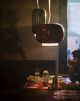 Person sitting at a table in a dimly lit room with a window in the background and a round and long suspension light from Foscarini hanging from the ceiling.