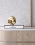 Decorative Chanel No. 5 bottle cap on a wooden surface with a textured wall background with a bronze sculpture