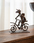 Bronze sculpture of a person on a bicycle with an umbrella on a wooden surface.
