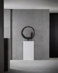 Modern sculpture on a pedestal against a gray wall in a minimalistic setting
