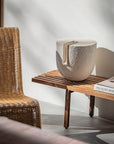 Wicker chair next to a wooden side table with a decorative sculpture from Gardeco and book against a white wall.