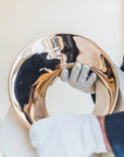 Gold decorative item being held by a person wearing gloves on a light background