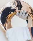 Gold decorative item being held by a person wearing gloves on a light background