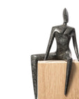 Bronze sculpture of a seated figure on a wooden base against a white background