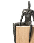 Bronze sculpture of a seated figure on a wooden base against a white background