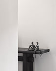 Two black sculptures of people sitting on a ledge against a white wall.