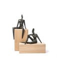 Two bronze sculptures of seated figures on wooden plinths against a white background
