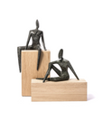Two bronze sculptures of seated figures on wooden plinths against a white background