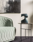 Modern interior with a quilted green sofa, abstract painting, and side table with sculpture.