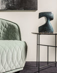 Modern interior with a quilted green sofa, abstract painting, and side table with sculpture.