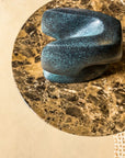 Blue green patina finish bronze sculpture on a circular marble-like surface with a beige background