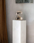 Bronze polished sculpture on a white pedestal against a neutral wall.
