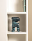 Blue abstract sculpture on a white shelf against a beige wall