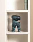 Blue abstract sculpture on a white shelf against a beige wall