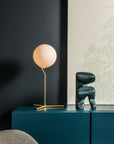 Modern interior with a table lamp and decorative object on a dark blue cabinet against a dark wall.