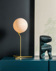 Modern interior with a table lamp and decorative object on a dark blue cabinet against a dark wall.