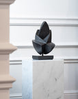 Abstract sculpture on a marble pedestal against a white wall.