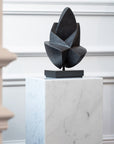 Abstract sculpture on a marble pedestal against a white wall.
