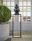 Decorative sculpture on a pedestal in a room with large windows and a plant.