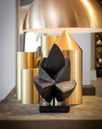 Decorative black sculpture on a wooden surface with gold lamp in the background