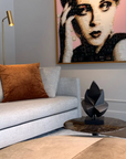 Living room with a gray sofa, brown pillow, and wall art of a woman's face and a black abstract bronze sculpture on a side table