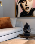 Living room with a gray sofa, brown pillow, and wall art of a woman's face and a black abstract bronze sculpture on a side table