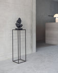 Modern interior with a black pedestal holding a decorative object against a gray wall.