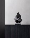 Black abstract sculpture on a dark wooden surface with a light gray wall background