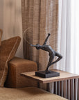 Bronze sculpture on a wooden side table next to a brown sofa with curtains in the background