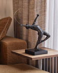 Bronze sculpture on a wooden side table next to a brown sofa with curtains in the background