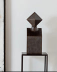 Abstract bronze sculpture on a stand against a neutral background
