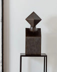 Abstract bronze sculpture on a stand against a neutral background