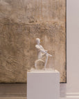 White ceramic sculpture on a pedestal against a textured wall.