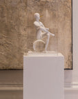 White ceramic sculpture on a pedestal against a textured wall.