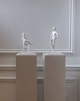 Two white sculptures - The Pinocchio & The Snob from Gardeco on pedestals against a plain wall