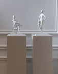 Two white sculptures - The Pinocchio & The Snob from Gardeco on pedestals against a plain wall