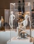 Sculpture of a seated figure with a glass ball inside, displayed in a clear case.