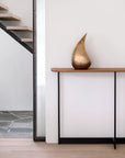 Modern interior with a gold sculpture on a wooden shelf next to a staircase.