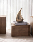 Bronze sculpture on a wooden pedestal with white curtains in the background