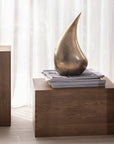 Bronze sculpture on a wooden pedestal with white curtains in the background