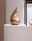 Bronze teardrop sculpture on a white surface with a blurred background