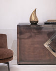Bronze sculpture on a reflective surface with a chair and books in the background