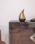 Bronze sculpture on a reflective surface with a chair and books in the background