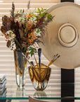 A contemporary refinement of the Gardeco Glass Vase Triangle 3 Fume Amber with bicolour glass, featuring Triangle design, filled with flowers and brushes.