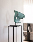 Green abstract sculpture on a black stand against a white wall