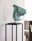 Green abstract sculpture on a black stand against a white wall